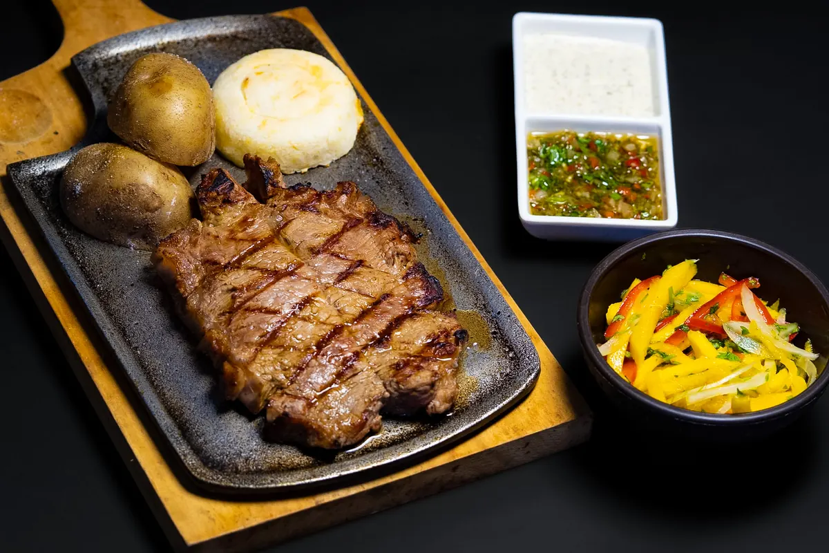 Corte de res marcado a la parrilla con papas, arepa, chimichurri y ensalada de mango