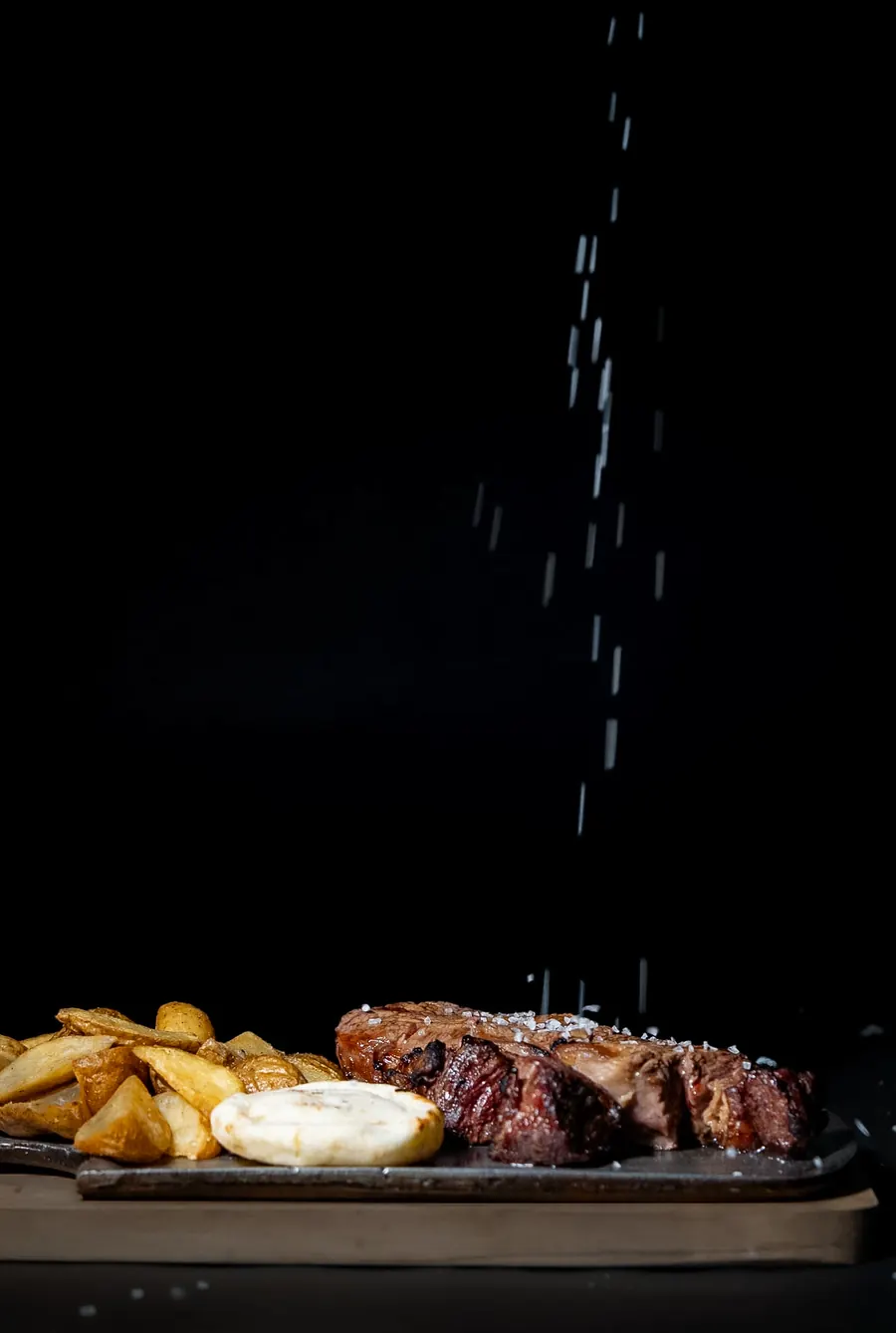 Corte de res a la parrilla con papas en cascos y arepa, mientras le cae sal gruesa